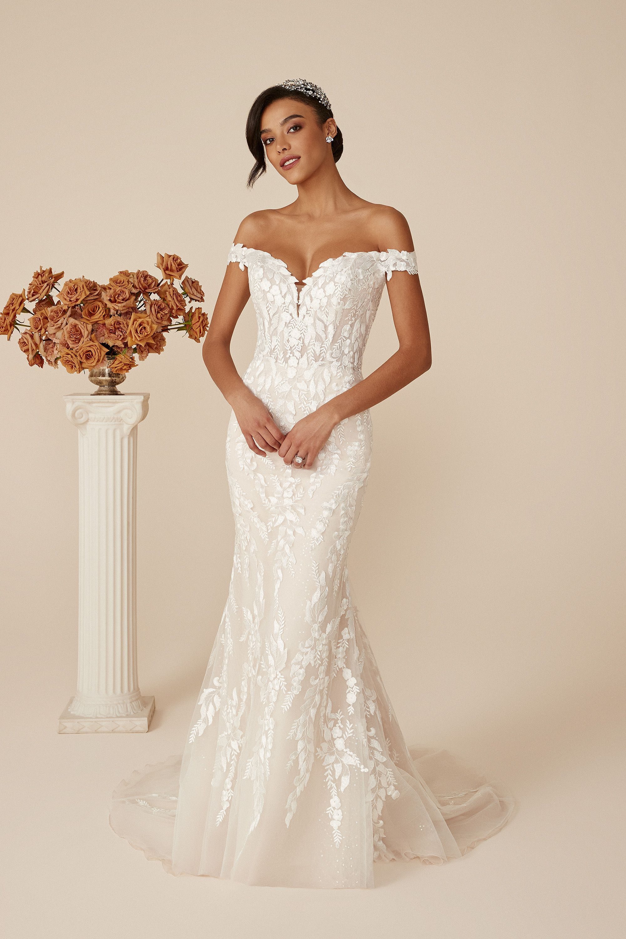 Deidra by Justin Alexander – A captivating off-the-shoulder mermaid wedding dress, this gown is adorned with exquisite floral lace appliqués that gracefully embellish the bodice and flow into the tulle skirt. The deep V-neckline and subtle illusion details add a touch of allure, while the fitted silhouette highlights the bride's figure, creating an elegant and timeless look.