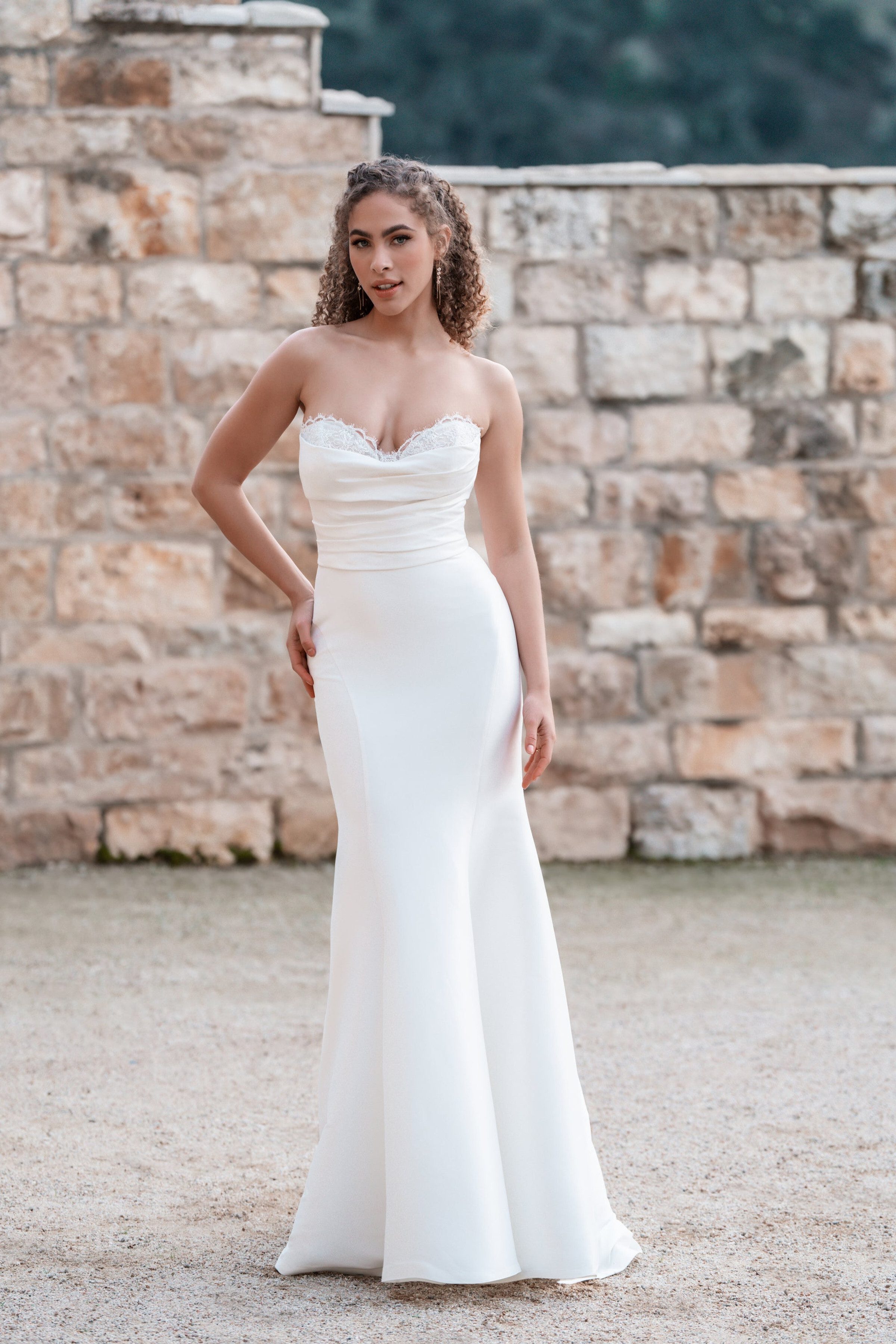 This Allure Bridals gown features a timeless strapless design with a sweetheart neckline accentuated by delicate lace trim. The fitted bodice with subtle ruching enhances the waist, flowing gracefully into a sleek, floor-length skirt that creates an elegant silhouette. The smooth fabric and minimalist style emphasize classic sophistication and understated beauty.