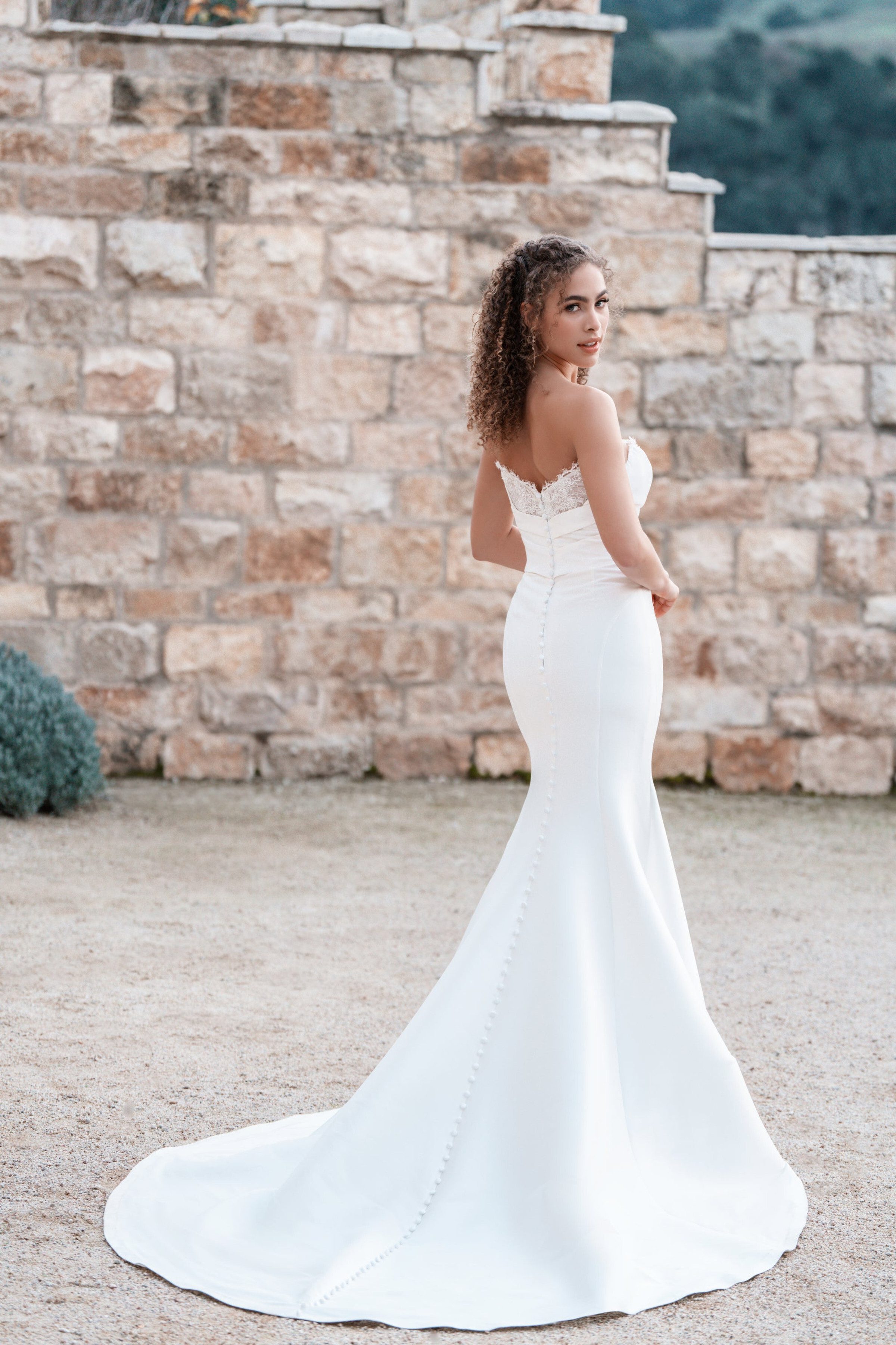 This Allure Bridals dress features a sophisticated strapless design with a lace-trimmed sweetheart neckline. The fitted bodice extends into a sleek, mermaid silhouette, accentuating the bride's curves. The back of the dress is adorned with a row of delicate buttons that run the length of the gown, adding a touch of classic elegance. The dress finishes with a dramatic, flowing train, creating a stunning and timeless bridal look.