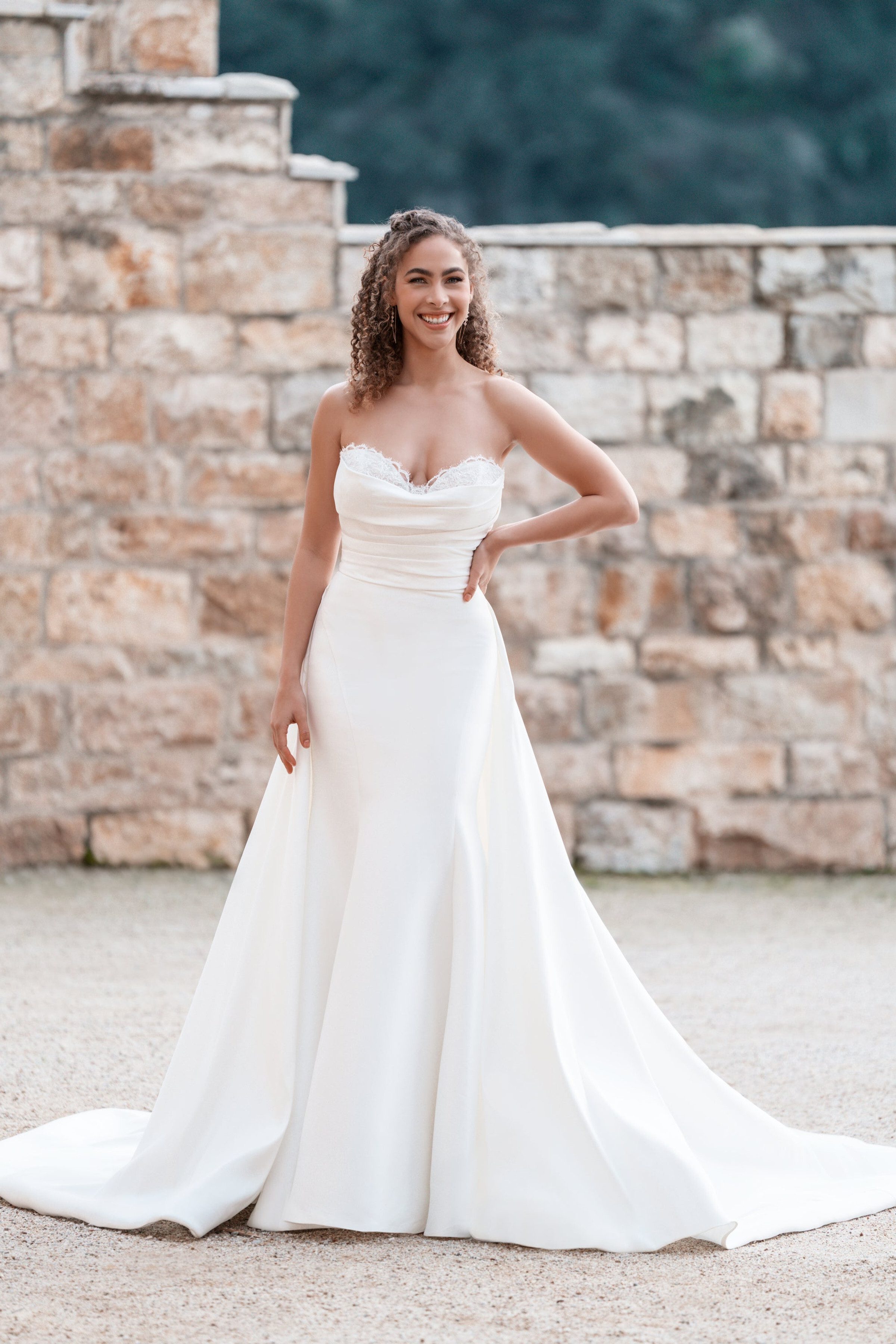 This Allure Bridals dress showcases a classic strapless design with a sweetheart neckline adorned with delicate lace trim. The bodice features subtle ruching that enhances the silhouette, leading into a smooth, fitted waist. The gown flows into a full A-line skirt, creating a timeless and elegant bridal look. The clean lines and minimalistic design emphasize sophistication and grace, perfect for a modern yet traditional bride.