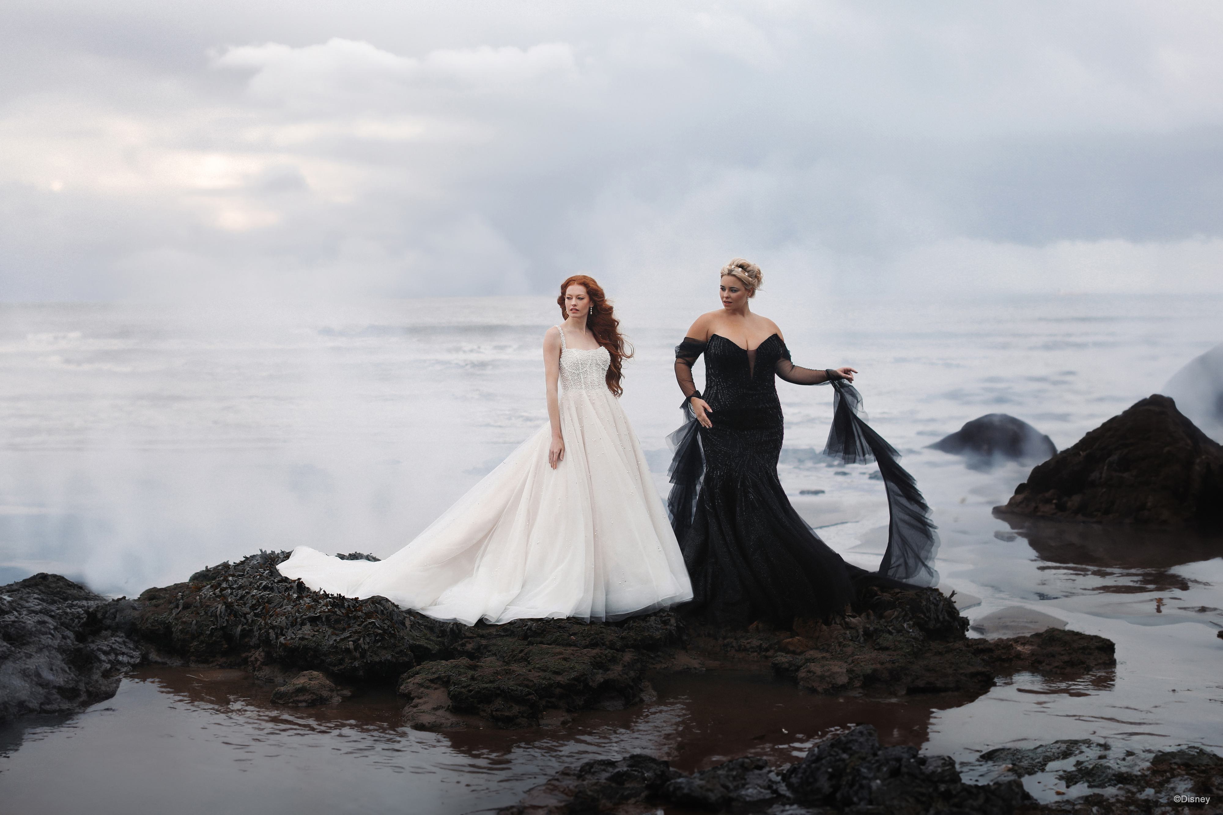 The image shows two women standing side by side, each wearing an elegant gown.
The woman on the left is dressed in a classic white wedding gown. The dress features a fitted bodice with short sleeves and a high neckline, likely adorned with lace. The skirt is full and voluminous, extending into a long train behind her, creating a traditional and romantic bridal look. Her long red hair is styled in loose waves, complementing the ethereal and timeless quality of the gown.
The woman on the right is wearing a striking black evening gown. The dress has an off-the-shoulder neckline, with a fitted bodice that accentuates her figure. The skirt flares out slightly and extends into a short train, adding to the gown's dramatic and sophisticated appearance. She is accessorizing with a black clutch and appears to have short, styled hair, enhancing the elegant and glamorous vibe of her ensemble.